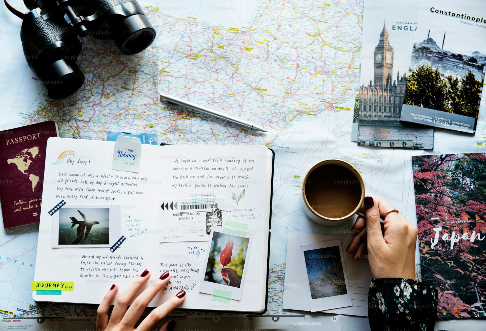 An open travel diary beside a laptop showing a travel blog, with a chai cup, map, and postcards on a wooden desk